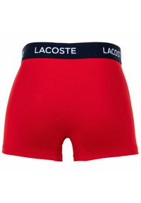 Piros férfi alsónadrág pamutból, sötétkék derékrésszel, rajta fehér "LACOSTE" logóval. Sima tapintású, a derék alatt illeszkedik.