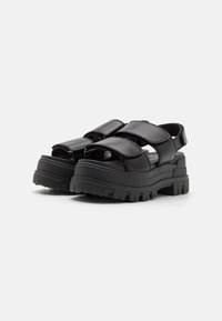 Black platform sandals with wide, adjustable straps, rugged textured sole, open toe design, and contrasting glossy finish on straps.