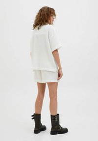 Conjunto de camiseta blanca texturizada y pantalones cortos hechos de un material ligero, combinado con botas negras de media pantorrilla con acentos metálicos y hebillas.