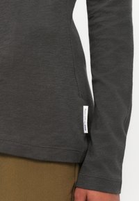Grijs shirt met lange mouwen, gemaakt van zachte stof, met een klassieke snit, subtiele stiksels en een klein merklabel aan de onderkant.