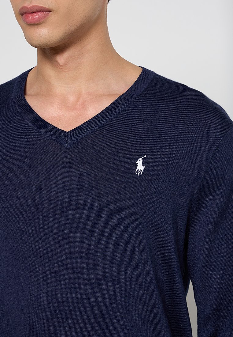 Maglione blu navy in cotone con scollatura a V, caratterizzato da una trama a coste e un piccolo logo ricamato bianco sul lato sinistro del petto.