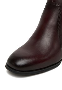 Pruun nahast saabas läikiva viimistlusega ja terava varbaga. Omab minimaalset õmblust ja sileda tekstuuriga. Must kummist tald.