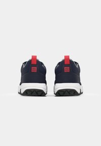 Paire de baskets noires avec semelles blanches vues de dos, avec languettes rouges et logo rouge Hugo sur le talon.
