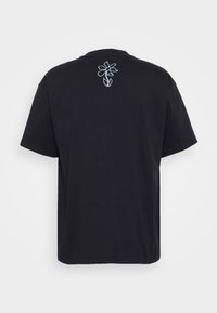 Zwarte korte mouwen t-shirt van katoen, met een blauwe geborduurde bloemenontwerp op de bovenrug. Eenvoudige ronde halslijn en een relaxed fit.