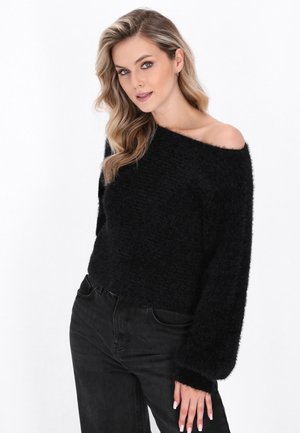 Zwarte, cropped sweater van zachte, gestructureerde stof met een off-shoulder ontwerp en volumineuze mouwen, gecombineerd met zwarte jeans.