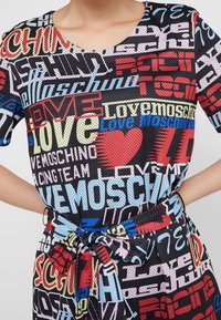 Vestido de malla negra con un estampado gráfico colorido que presenta las palabras "Love Moschino" en varias tipografías y colores. Tiene un detalle de cintura atada.