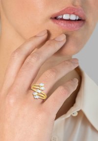 Bague en or avec trois gemmes ovales, présentant un design fendu. La bague a une texture lisse et une finition brillante, posée sur une main près du visage.