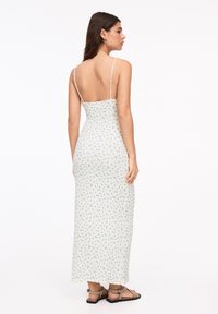Rochie maxi cu bretele subțiri, fabricată dintr-un material crem deschis cu modele florale verzi mici, bust ajustat și design cu spate descoperit.