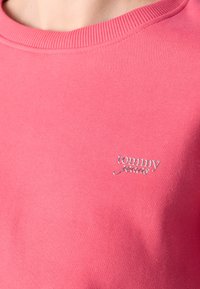 Pink sweatshirt made of cotton, featuring a round neckline and a small silver "tommy jeans" logo on the chest. Smooth texture.