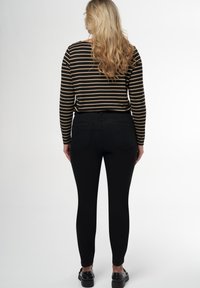 Un pantalon skinny noir associé à une chemise à rayures noire et beige à manches longues, montrant une vue arrière avec des poches visibles et un tissu lisse.