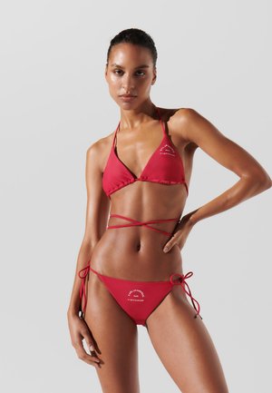 Crveni bikinijski set koji sadrži trokutasti halter top s podesivim trakama i vezanjem, visokim stranicama i suptilnim brendiranjem na donjem dijelu.