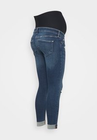 Jeans de maternidad con una tela de denim azul oscuro. Cintura alta de elástico negro, corte skinny y detalles desgastados en los bolsillos traseros.