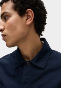 Granatowa koszula zapinana na guziki z kołnierzykiem, o strukturalnym fasonie i gładkiej fakturze. Posiada jeden guzik przy szyi oraz przeszycia.