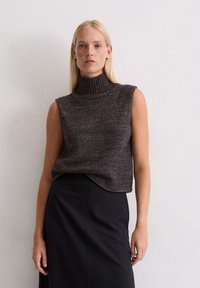 Mouwloze turtleneck top in donkergrijs gemêleerd breiwerk, met een hoge kraag en een ontspannen pasvorm, gecombineerd met een zwarte rok.