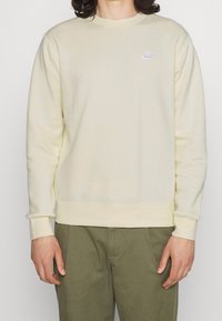 Sudadera de un amarillo claro, fabricada con una tela suave, que presenta un cuello redondo, mangas largas y un pequeño logo de Nike blanco en el pecho.