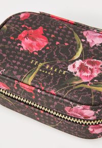 Pequeño estuche rectangular con cremallera con flores rosas y rojas sobre un fondo negro texturizado, cremallera dorada y "Ted Baker London" grabado en dorado.