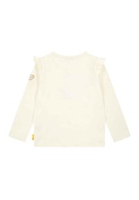 Camicia a maniche lunghe color crema con dettagli a volant sulle spalle e una piccola patch di un orsetto sulla manica sinistra. Realizzata in morbido cotone.