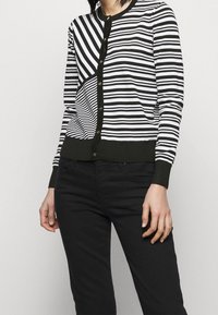 Zwart-wit gestreepte cardigan met een knoopsluiting, met verschillende strookbreedtes en een contrasterende donkergroene zoom en manchetten.