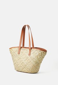 Flätad halm tote-väska med ljusbruna läderdetaljer och handtag. Den har en rymlig design och en strukturerad form för enkel bärning.