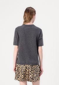 Grauer Wollmischpullover mit kurzen Ärmeln und rundem Ausschnitt, getragen über einem gemusterten beige-schwarzen Leo-Print-Rock.