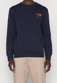 Tmavě modrá mikina z bavlněné směsi, s žebrovanými manžetami a lemem, s vícebarevným logem "ESP RIT" na hrudi.