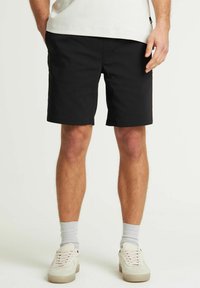 Zwarte shorts met een rechte snit, gemaakt van lichtgewichtmateriaal. Voorzien van voorzakken en een nette zoom. D gedragen met lichtgekleurde sneakers en sokken.