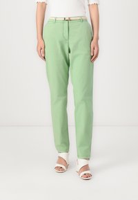 Green cotton trousers with a tailored fit, featuring a front zipper, belt loops, and side pockets. Styled with a neutral belt and white sandals.