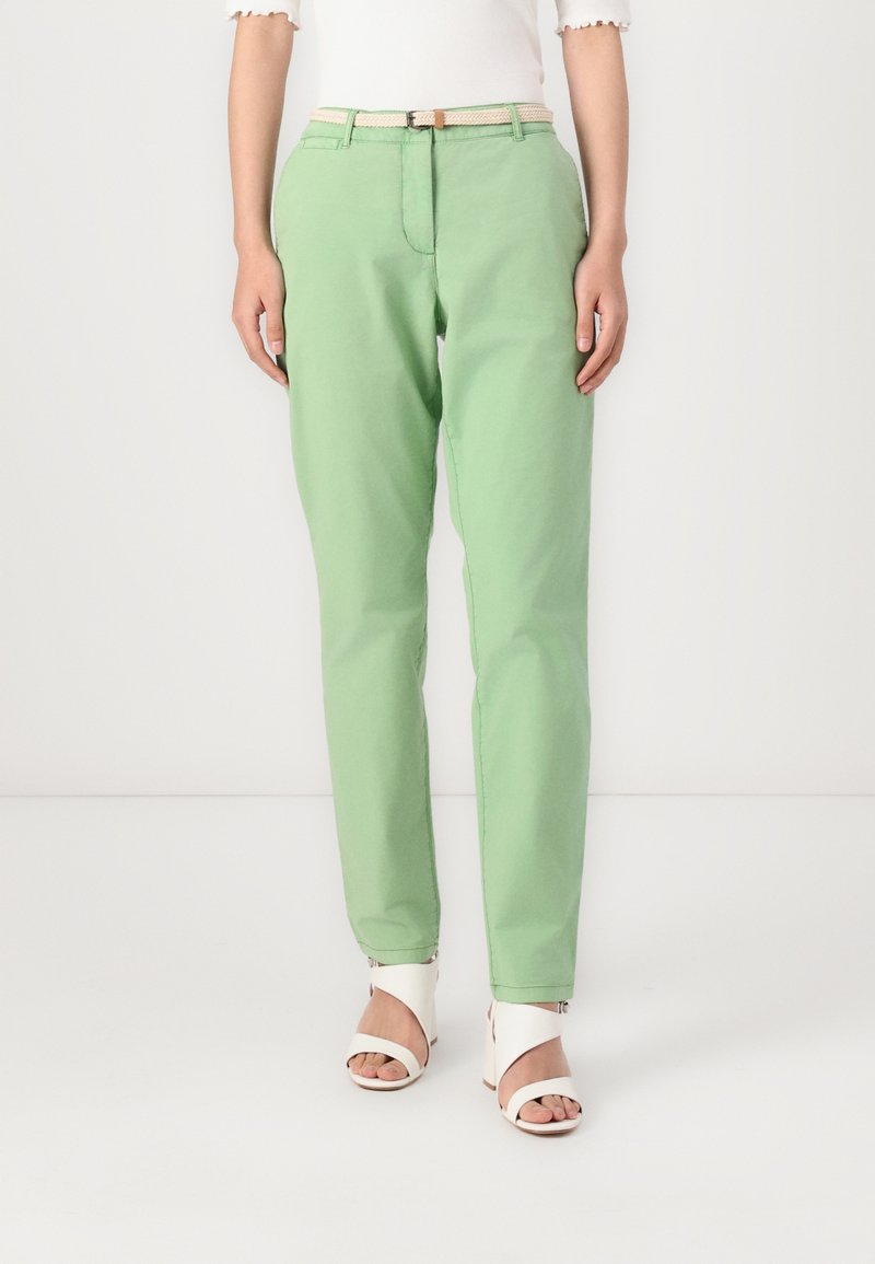 Green cotton trousers with a tailored fit, featuring a front zipper, belt loops, and side pockets. Styled with a neutral belt and white sandals.