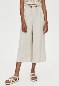 Pantalons en lin beige à jambes larges et taille à cordon. Texture lisse et longueur courte. Assortis à des sandales tressées à lanières.