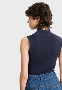 Ärmlös marinblå ribbad topp med hög krage, tillsammans med högmidjade blå denimshorts med bakfickor och synliga sömmar.