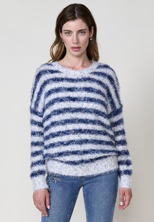 Suéter rayado difuso en azul claro y marino, con un corte holgado, escote ancho y textura contrastante. Combinado con unos jeans de mezclilla.