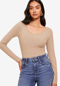 Beige hosszú ujjú bodysuit bordázott textúrával �és kereknyakú fazonnal, világoskék, magas derekú farmernadrággal, elülső zsebekkel párosítva.