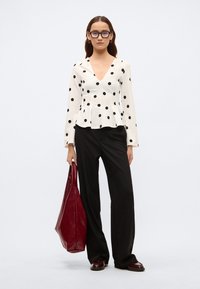 Langermet hvit bluse med svarte polkadotter, V-hals, peplum i midjen, kombinert med svarte vide bukser og en burgunder storveske.
