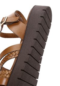 Sandalo in pelle marrone con dettagli in fascia intrecciata, suola piatta in gomma nera con battistrada diagonale per la trazione e hardware con fibbia regolabile.