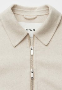 Beige wool blend jacket with a collar and a silver metallic zip. The fabric has a soft texture, designed for a relaxed fit.