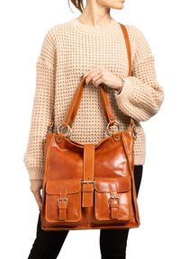 Bruine leren handtas met twee voorkleppen, gouden hardware-accenten en een brede schouderband. Glad textuur, rechthoekige vorm en centrale klep sluiting.