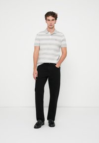 Polo de rayas en gris y blanco, de manga corta, con cuello; combinado con pantalones negros y zapatos negros; diseño minimalista.