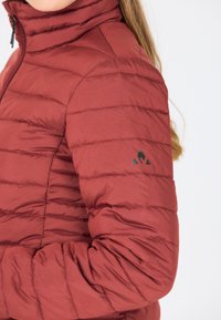 Rød pufferjakke med vandret syninger, høj krave og sort logoaccent på venstre ærme. Glat, let stoftekstur.