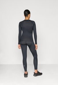 Czarna, długosleeve'owa odzież sportowa w zestawie z dopasowanymi czarnymi legginsami. Top ma okrągły dekolt i bezszwowy design; legginsy posiadają detal z logo.