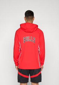 Rød hettegenser med "BULLS" i svart skrift på baksiden, hvite side-striper og hette. Båret med svarte shorts med røde detaljer.