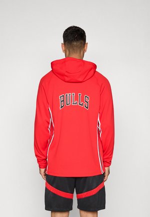Punainen huppari, jossa on mustalla kirjoitettu "BULLS" selässä, valkoiset sivuraitat ja huppu. Yhdistetty mustiin shortseihin, joissa on punaisia yksityiskohtia.