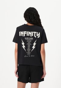 Sort kortærmet t-shirt med et grafisk print på ryggen, der viser ordet "INFINITY" og forskellige bynavne, accentueret af lyn.