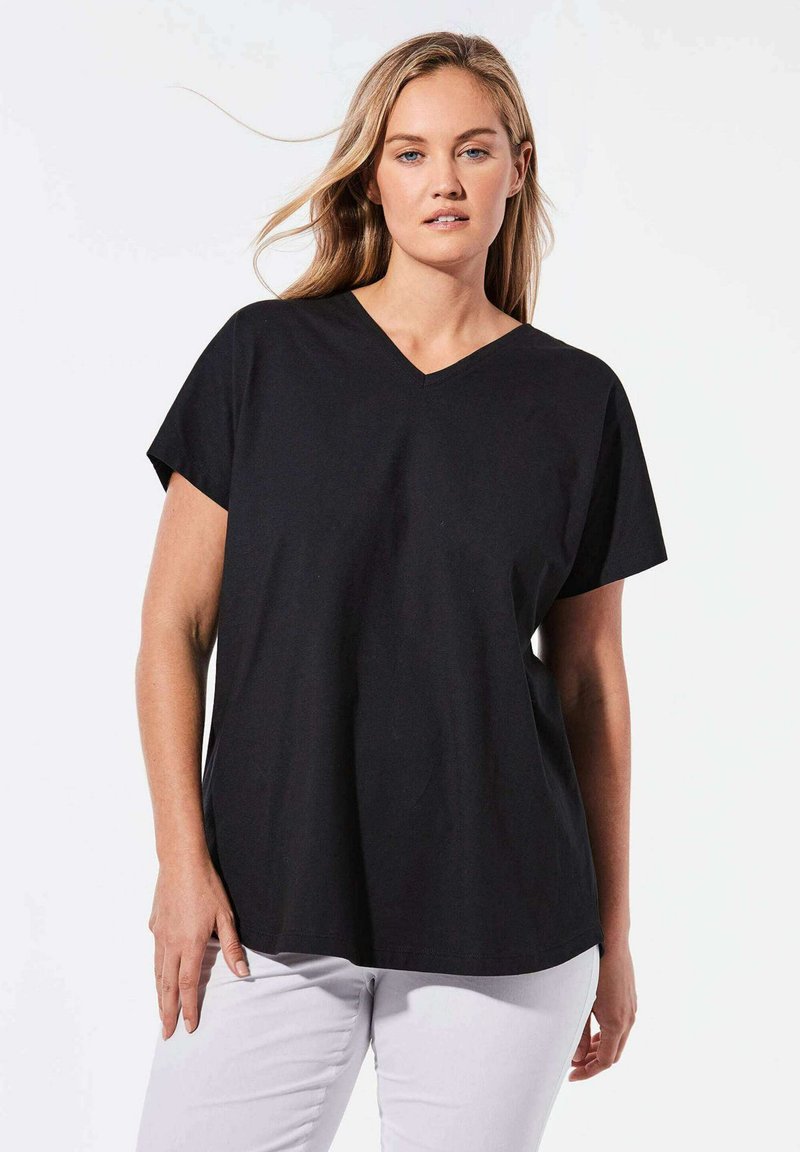 Schwarzes V-Ausschnitt-T-Shirt aus weicher Baumwolle. Kurze Ärmel in Cap-Form, entspannter Schnitt und glatte Textur. Kombiniert mit weißen Hosen.