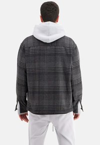 Rutet oversized jakke i sort og grå stof, med hætte i hvid, lange ærmer og sideslidser for ekstra komfort og stil.