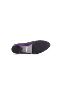 Chaussure en daim violette avec un petit talon, semelle en caoutchouc, détail de fausse fermeture éclair et marquage métallique sur une semelle intérieure grise. Présente un bout arrondi.