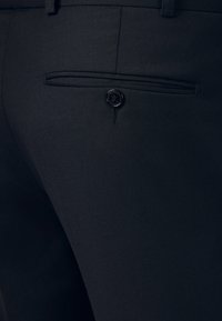 Czarne spodnie o dopasowanym kroju, z tylną kieszenią z pojedynczym czarnym guzikiem i subtelną fakturą materiału. Starannie zszyte krawędzie.