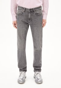 Graue Jeans aus Denim mit geradem Bein, ausgestattet mit Fronttaschen und subtilen Nähdetails. Getragen mit einem hellrosa Langarmshirt.