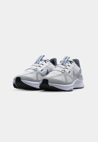 Nike løpesko i grå og hvit, med overdel i mesh, teksturert stoff, lisser og såle i sort gummi med blå detaljer.
