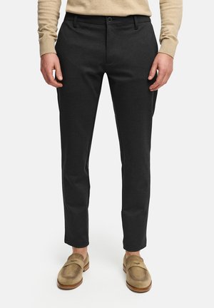 Pantalones negros con un corte ajustado, textura suave, cierre de botón, bolsillos laterales y diseño hasta el tobillo, combinados con mocasines beige.