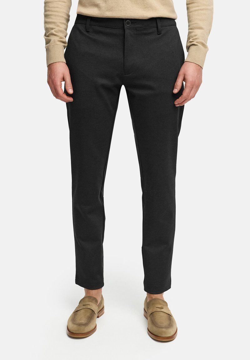 Pantalones negros con un corte ajustado, textura suave, cierre de botón, bolsillos laterales y diseño hasta el tobillo, combinados con mocasines beige.